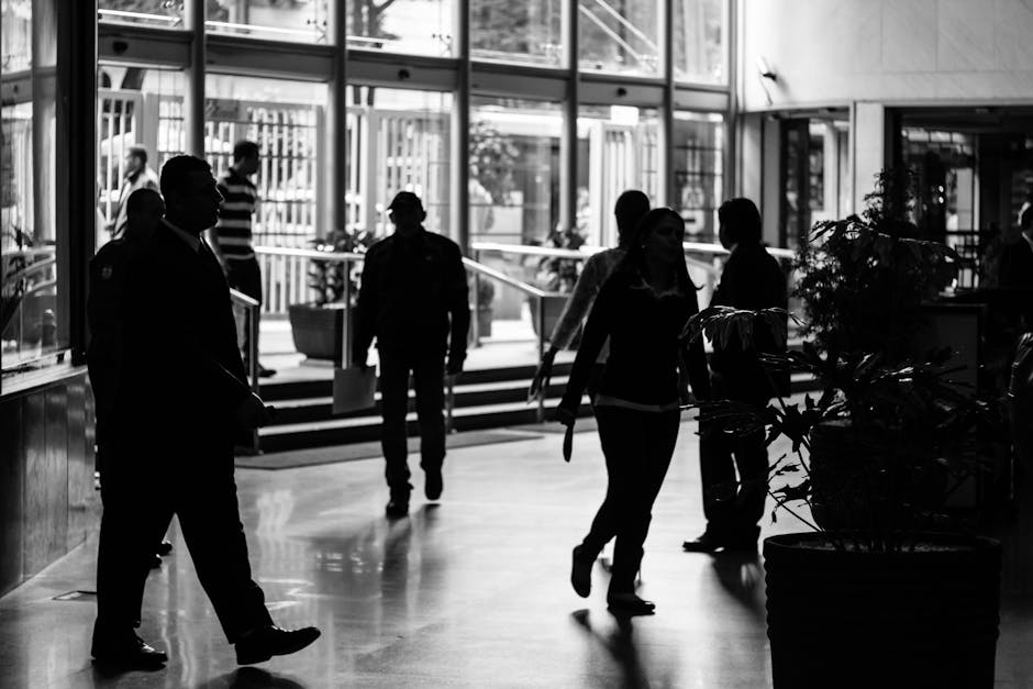 Silhouetted figures walk through a busy indoor lobby in a black and white composition.